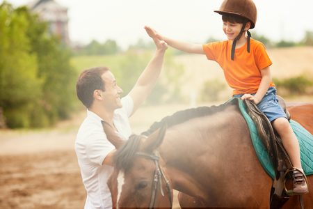 young boy with helmet on horse receiving high five from adult